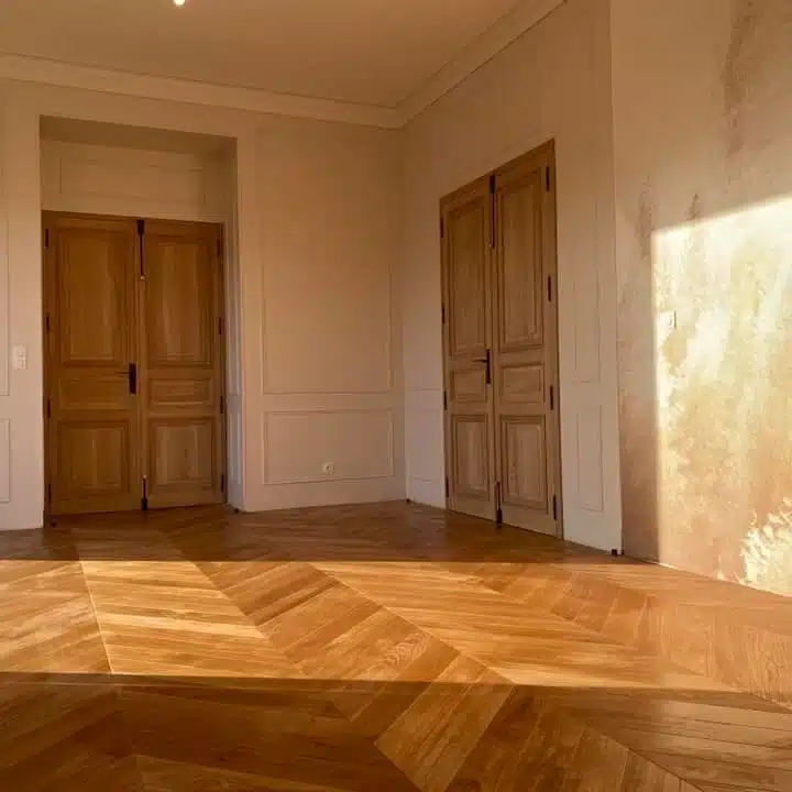 Pièce lumineuse avec parquet en chevrons et portes en bois massif, mettant en avant l’élégance et la qualité de la menuiserie intérieure traditionnelle.