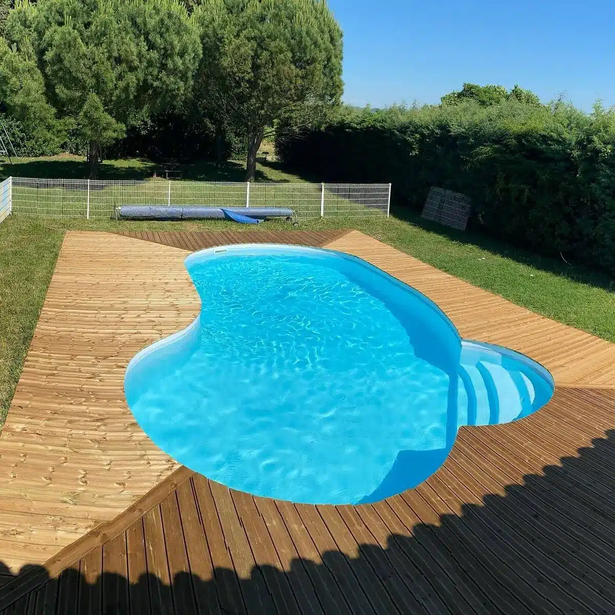 Vue complète d'une piscine entourée d'une terrasse en bois, créant un espace élégant et naturel dans un jardin verdoyant.