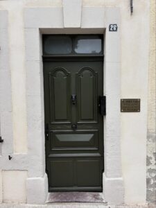 Entrée d'un cabinet médical : porte verte foncée avec heurtoir main, encadrement blanc, plaque "Dr. DIDIER Nicolas Médecine Générale 26".