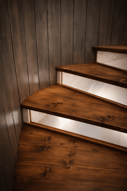 Escalier en bois sombre avec marches rétroéclairées contre un mur lambrissé.