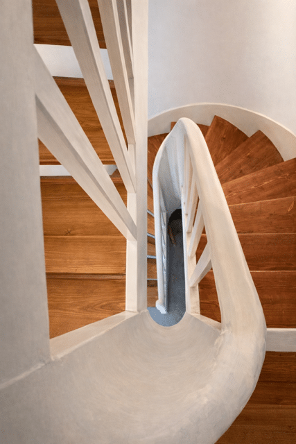 Escalier en Colimaçon : Marches Bois et Design Blanc Vue plongeante d'un escalier en colimaçon avec marches en bois et garde-corps blanc incurvé.