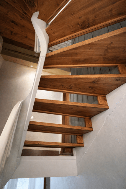 Escalier en colimaçon en bois brun et support blanc incurvé, vue en contre-plongée.