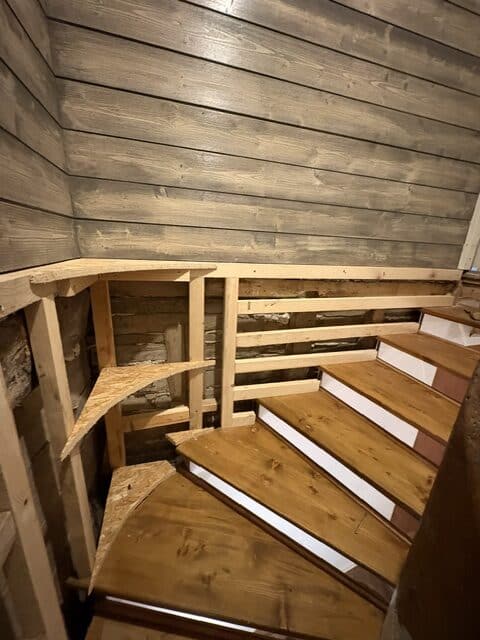 Escalier tournant en bois en rénovation, ossature murale apparente dans un chalet.