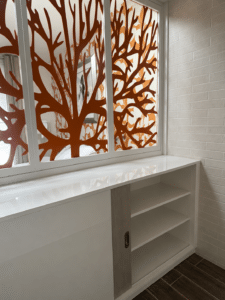 Meuble de rangement blanc sous une verrière décorative orange au motif corail, contre un mur de briques blanches.
