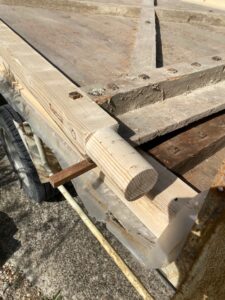 Tenon cylindrique sur poutre en bois clair posée sur une remorque de chantier.